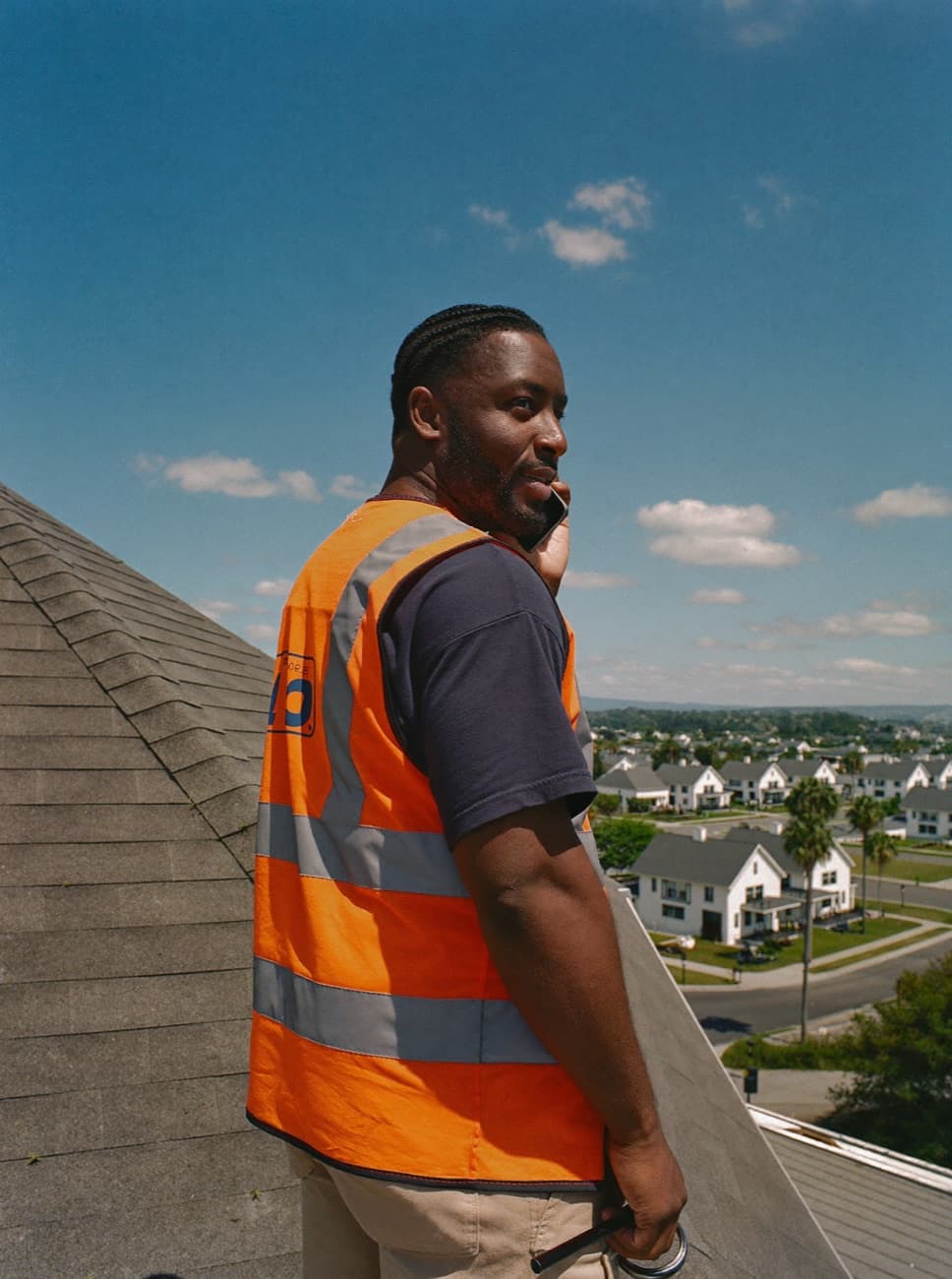 Roofing contractor on a sunlit shingle roof taking a customer call